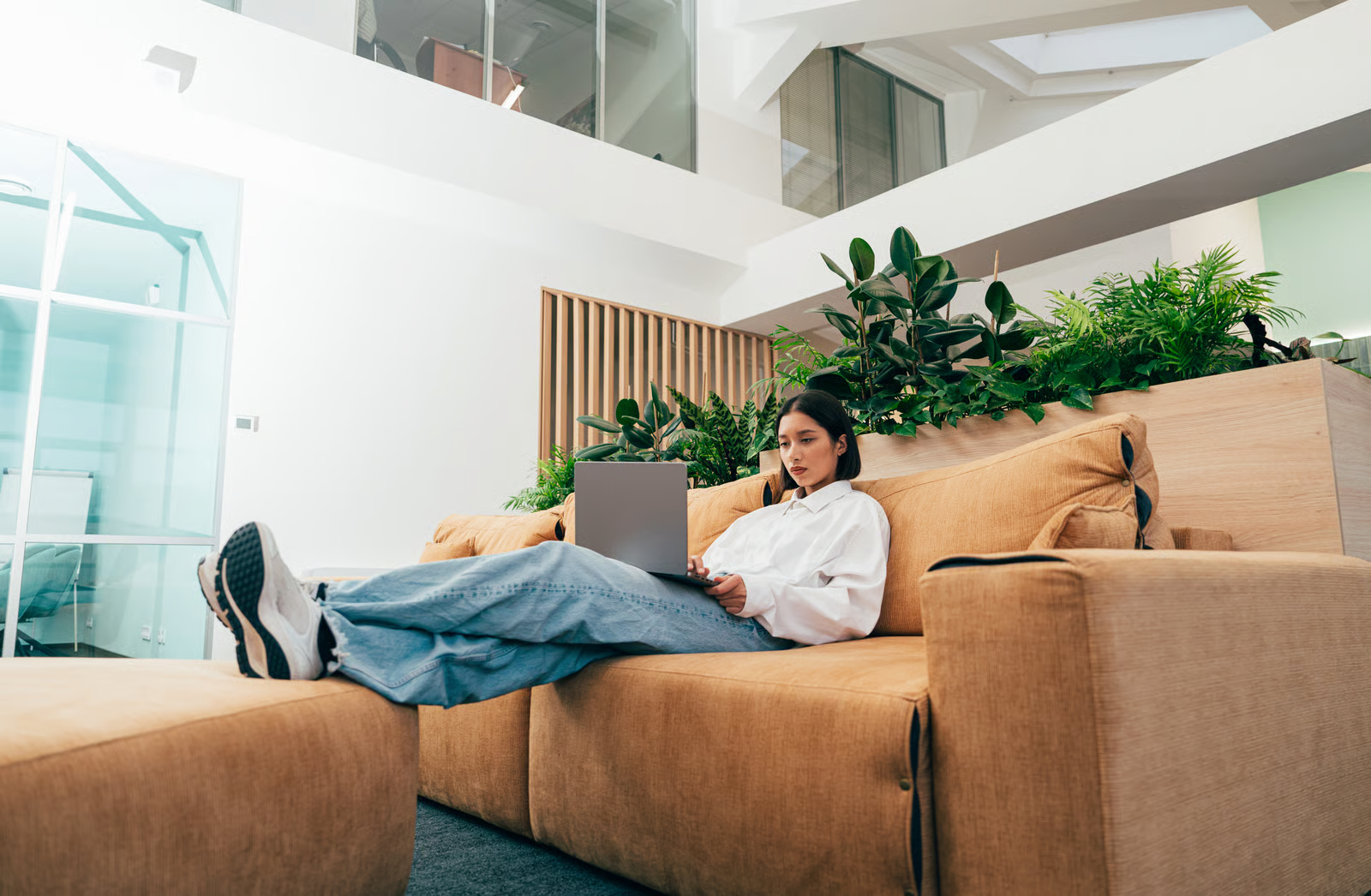 Femme assise sur un canapé orange travaillant sur son ordinateur portable